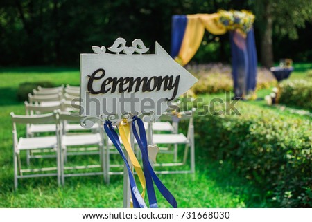 Beautiful settings for outdoors wedding ceremony and celebration. Blurry beautifully decorated arch with yellow and blue fabric and bouquets of flowers in background. Horizontal photography.