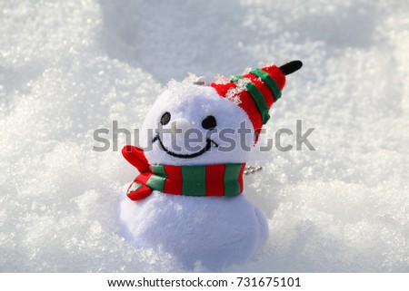 Smiling Christmas Snowman toy dressed in scarf and hat on white snow in sunny day.