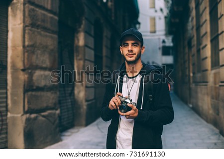 Attractive young man, student or freelance photographer smiles and laughs into camera, explores historic center of city or village, urban adventurer nomad travels the world Royalty-Free Stock Photo #731691130