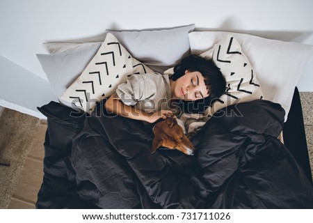 Beautiful young woman or girl cuddles and hugs her best friend basenji puppy dog, sleep together under blankets in hipster designer bed on cold day, peace and quiet Royalty-Free Stock Photo #731711026