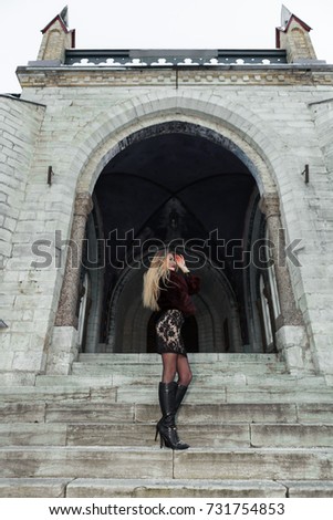 Young girl dressed fur coat and dress standing on the stairs of church. Old church on the background.