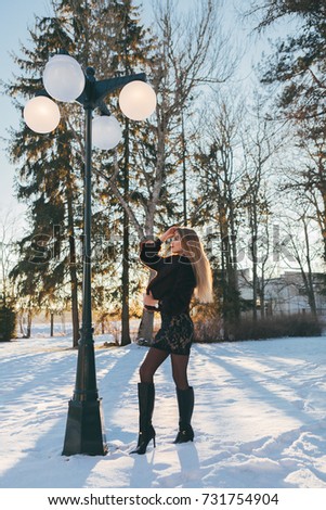Awesome model with red lips under street light posing and look in the sky. Sunlight on the background. Snow around.
