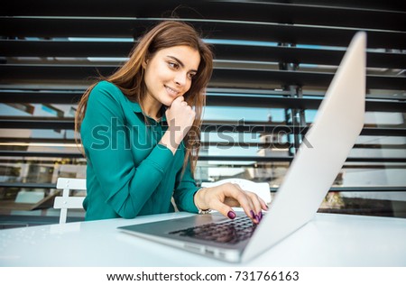 Beautiful student girl works with laptop computer outdoors before moder building wall
