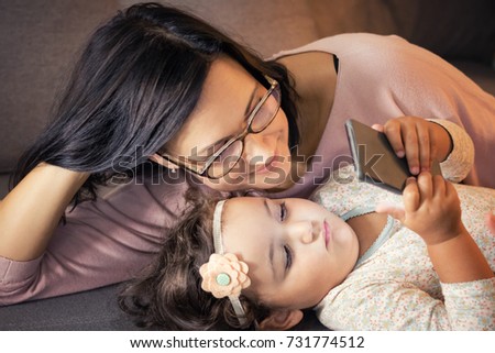 Happy mother and her small daughter using mobile phone while relaxing at home. 