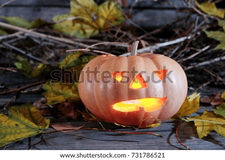 Halloween pumpkin head on a wooden background and yellow autumn leaves