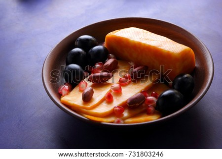 Orange cheese, sliced cheese, a sort of hard cheese, marbled cheese, dark blue grapes, peanuts and pomegranate seeds in a clay plate on a dark blue background in retro style