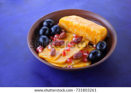Orange cheese, sliced cheese, a sort of hard cheese, marbled cheese, dark blue grapes, peanuts and pomegranate seeds in a clay plate on a dark blue background in retro style