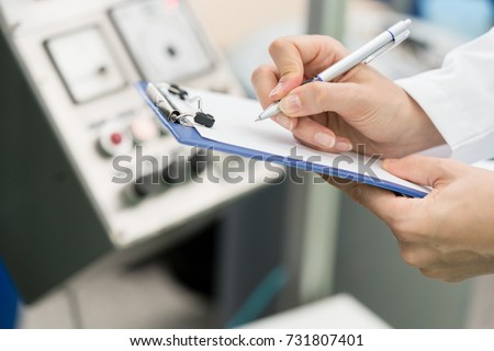 Side view close-up of the hands of a female engineer or inspector, ready for writing a technical report about the manufacturing process in a contemporary factory Royalty-Free Stock Photo #731807401