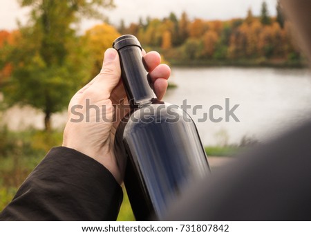 Bottle of red wine in the hands of a man in a black cloak.