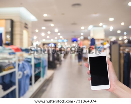 Hand holding mobile phone with blurred image of department store or shopping mall, Internet, Social media