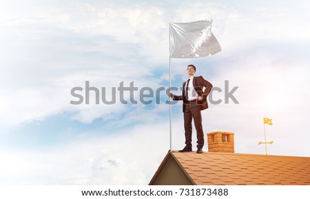 Businessman standing on house roof and holding white flag. Mixed media