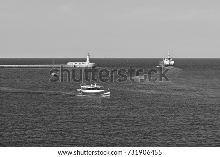 Cargo ship leaves the harbor of Valletta. Lighthouses indicate the entrance to the ports of Malta. Pleasure craft in the bay basin. Black and white picture