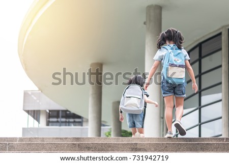 Back to school education concept with girl kids (elementary students) carrying backpacks going, running to class on school first day and walking up building stair happily Royalty-Free Stock Photo #731942719