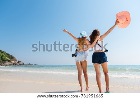 Portrait of two young asian female friends walking on the sea shore turn back at camera laughing. Multiracial young women strolling along a beach.