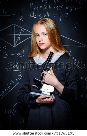 Education. Smart student girl wearing black school dress standing by a blackboard. Chalkboard background.