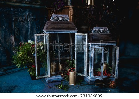 dark decor with dried flowers, vases, chandeliers, textured fabrics against the wall with a golden frame, a wooden table in a luxurious royal Victorian style, candles in old lanterns