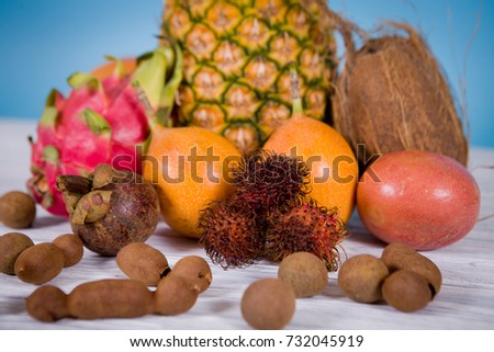 On blue wooden table background a composition made of fruits from Thailand. Coconut, pineapple, mango, rambutan, passion fruit, pithaya, papaya, kumquat, granadila