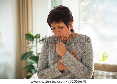 Sick mature woman with sore throat, standing in living room at home. Catching cold, having cough. Royalty-Free Stock Photo #732055678