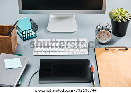 The gray desk with laptop, notepad with blank sheet, pot of flower, stylus and tablet for retouching
