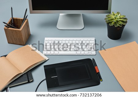 The gray desk with laptop, notepad with blank sheet, pot of flower, stylus and tablet for retouching