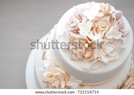 Three-tiered white wedding cake decorated with flowers from mastic on a white wooden table. Picture for a menu or a confectionery catalog. Top view.