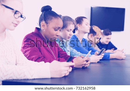Male and female students playing with their smartphones in school