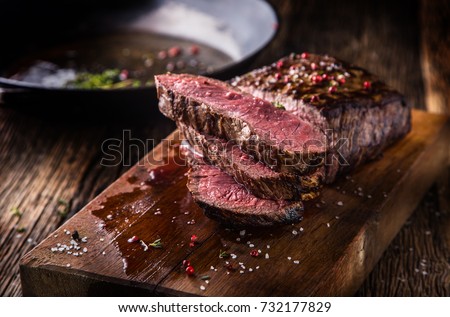 Juicy medium Beef Rib Eye steak slices in pan on wooden board with fork and knife herbs spices and salt. Royalty-Free Stock Photo #732177829