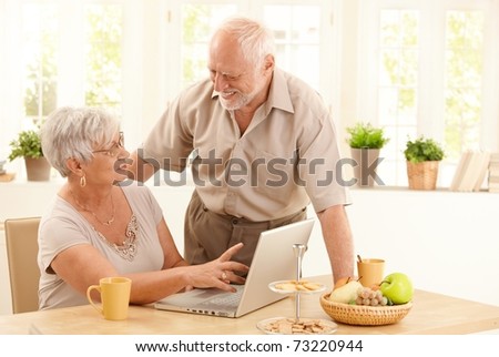 Happy senior couple using laptop computer at home, wife pointing at screen, husband laughing at wife.?