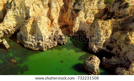 Aerial shot of colorful landscape with white rough cliffs of tropical ocean coastline and green water of calm lagoon, Portugal, Algarve.
