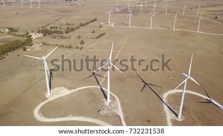 Aerial shot of sandy desert with placed rows of white windmills creating electrical power in bright tropical sunlight.