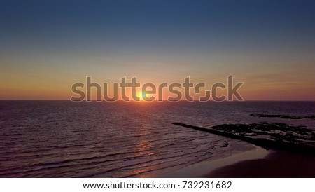 Aerial shot of breathtaking view with calm ocean waves on background of colorful sky and sun rising above water.
