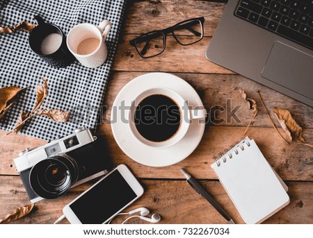 coffee cup on wooden table with retro camera, smartphone, notebook, laptop and dry leaf in the coffee shop.