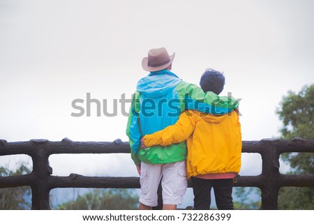 Happy senior couple watching sunrise and take the photo by camera over the mountain in winter, is covered with fog.