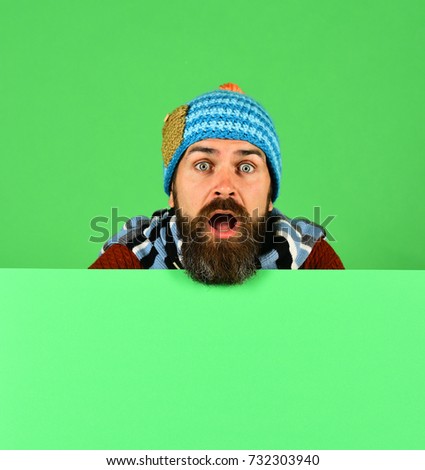 Man in warm hat on green background, copy space. Autumn and demi season clothes concept. October and November sale idea. Hipster with beard and surprised face wears warm clothes