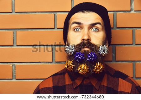 Bearded man, long beard. Brutal caucasian surprised hipster with colorful gift decoration stars in moustache, wearing red black checkered shirt on brown brick wall studio background