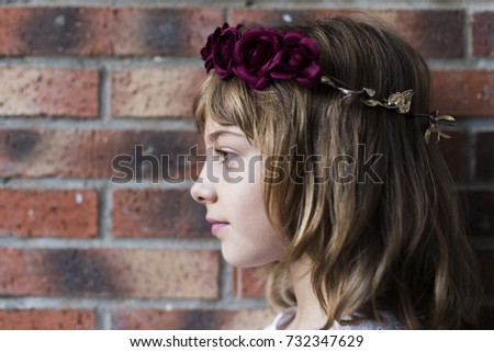 portrait of a beautiful little girl wearing a red wreath roses on her head. Brick background. Lifestyle