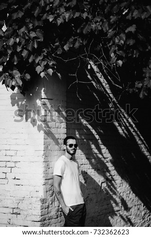Young stylish man wearing white blank t-shirt with beard in glasses, standing on the street on city background. Street photo