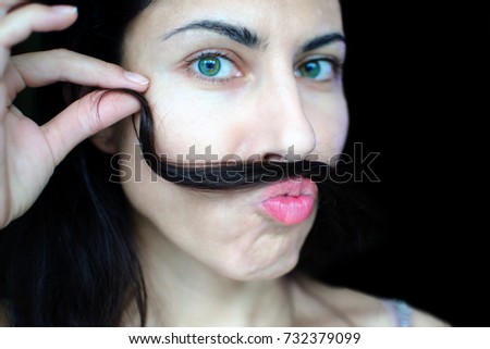 Portrait of a young beautiful woman with dark hair holding a strand of her hair over her upper lip. The concept of the problem of removing excess hair on the face of women. Funny face.