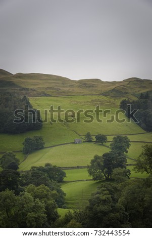 Old barn in green fields on hillside with moody sky England