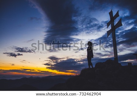 Silhouette of young woman under cross with  dark summer sunrise