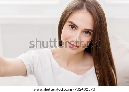 Young smiling woman making selfie, long-haired brunette in white clothes, closeup