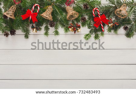 Xmas decoration border background. Fir tree branches border with bells, candy canes and pine cones top view with copy space on white wooden table. Christmas ornaments frame for any winter holiday