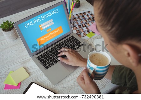 Online banking text on blue log in display against female photo editor holding coffee cup while using laptop