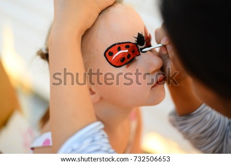 a little girl on her face draw a picture of ladybug