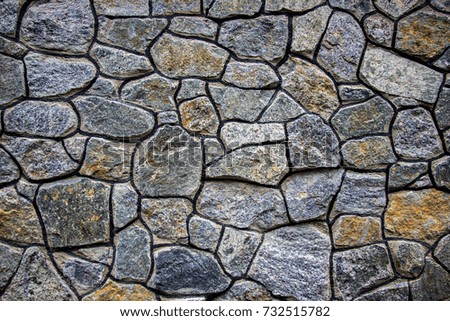 Large wall of natural granite stones of different size and color gray texture on a summer day
