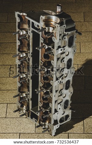 A 16V aluminum cylinder head on the floor with brown tiles, like in a workshop or similar place.