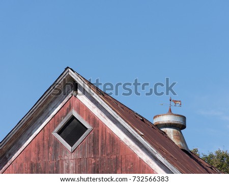 Close up of a vintage weather vane with a cow and arrow made of metal on top of a rustic weathered red barn roof. Image has copy space.