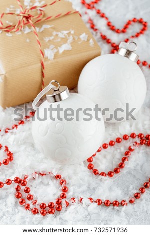 Christmas gift boxes in kraft paper, red beads, white Christmas balls and fir branches on a snow-covered background