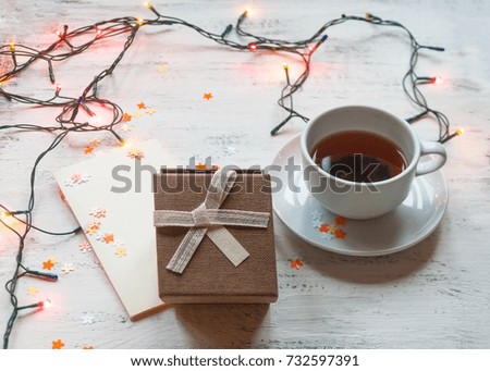 A cup of tea, a Christmas garland with lights and a gift box on a light background. A Christmas gift