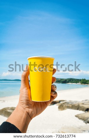 Female hand holding yellow cup with cool word  sea and blue sky background ,concept time to vacation